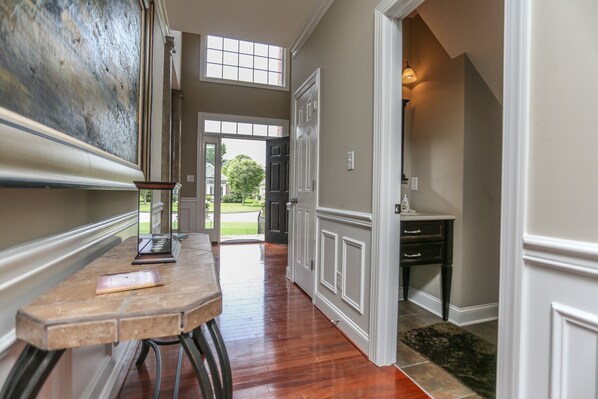 A hallway with a wooden floor, a table with a book, and a door leading to a garden. - Beautiful 2 story brick home on a cul-de-sac. A beautiful pond in the back yard (Poquoson)