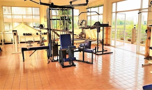 A gym with various exercise equipment, large windows, and a view of greenery outside.