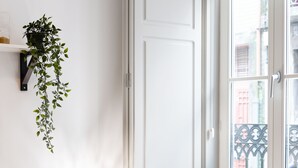 Un salon moderne avec un téléviseur, un canapé, une plante suspendue et une fenêtre donnant sur des immeubles.