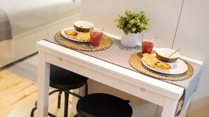 Une petite table à manger avec un plateau blanc, deux tabourets noirs et une plante en pot.