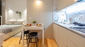 Une cuisine moderne dotée d’une cuisinière intégrée, un coin repas avec une table et des chaises, et un lit avec un mur décoré d’un motif en chevrons.