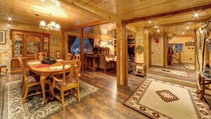 A wooden interior with a dining area, a fireplace, and a view through a window.