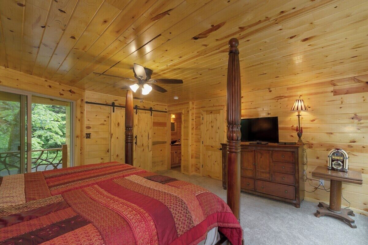 Une chambre dans un chalet en bois, avec un lit, un ventilateur de plafond, une télévision et une commode.