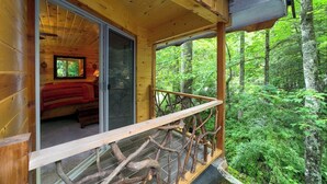 A wooden cabin with a glass door leading to a bedroom with a bed and a nightstand.