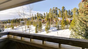 A view from a balcony with a wooden railing, overlooking a snowy landscape with trees and buildings. - Chic & Cozy Breck Condo: Ski-In/Ski-Out at Peak 8! (Breckenridge)
