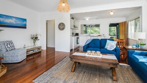 A spacious living room with a blue sofa, a wooden coffee table, and a kitchen in the background. - Salt Breeze - upstairs only (Lake Cathie)