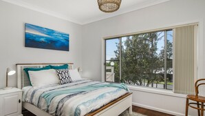 A bedroom with a large window, a bed with a blue and white striped bedspread, a nightstand, and a chair. - Salt Breeze - upstairs only (Lake Cathie)