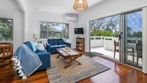 A spacious living room with a blue sofa, a wooden coffee table, and a large window overlooking a balcony. - Salt Breeze - upstairs only (Lake Cathie)