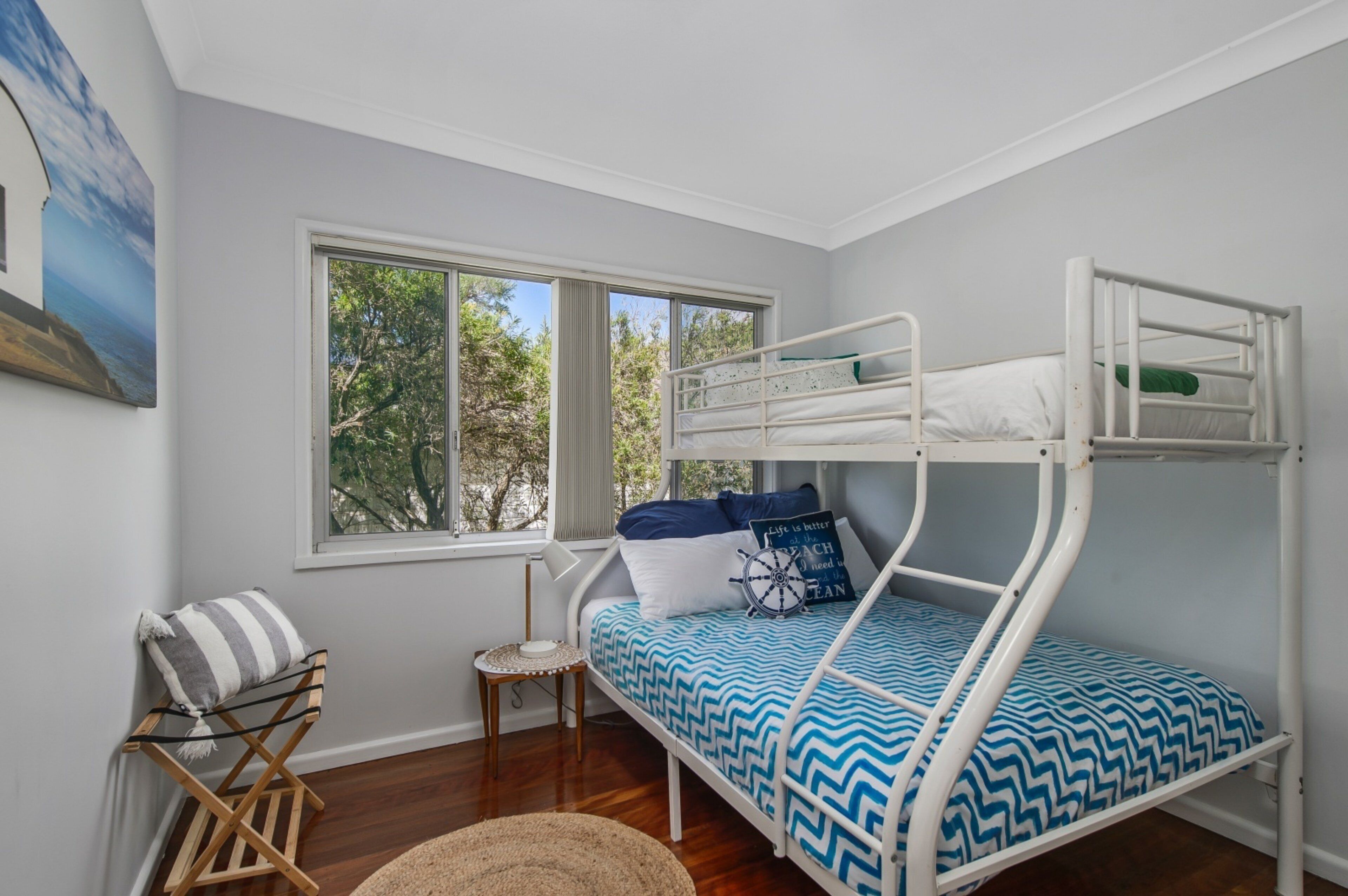 Un lit superposé avec une couvre-lit à motifs bleus et blancs, une petite table d’appoint, une chaise et une fenêtre donnant sur des arbres.