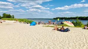 A beach with people sunbathing and swimming, a tent, and a colorful umbrella.