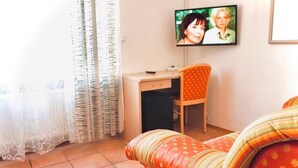 A living room with a sofa, a television mounted on the wall, a desk, and a chair. - Hotel Romina (Frankfurt)