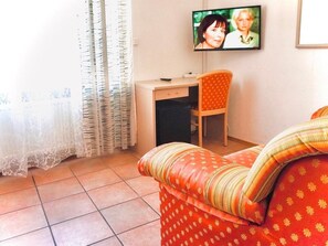 Een woonkamer met een bank, een aan de muur bevestigde televisie, een bureau en een stoel.