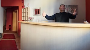 A hotel reception desk with a red carpet, a vase, and a framed picture on the wall. - Hotel Romina (Frankfurt)