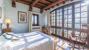 A bedroom with a large window, a bed with a quilt, a chair, and a desk. - Il Roseto 10, Emma Villas (La Costa)