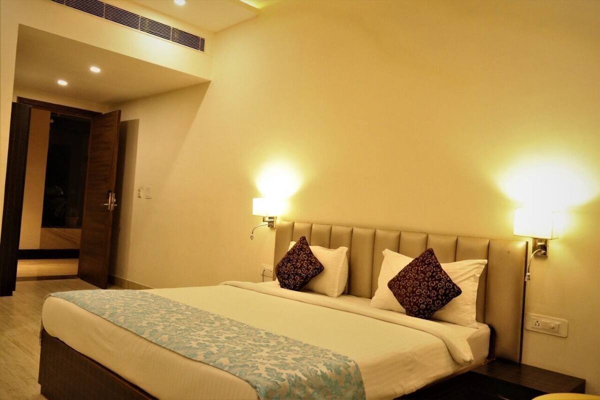 A hotel room with a large bed, two wall-mounted lamps, and a door leading to a bathroom.