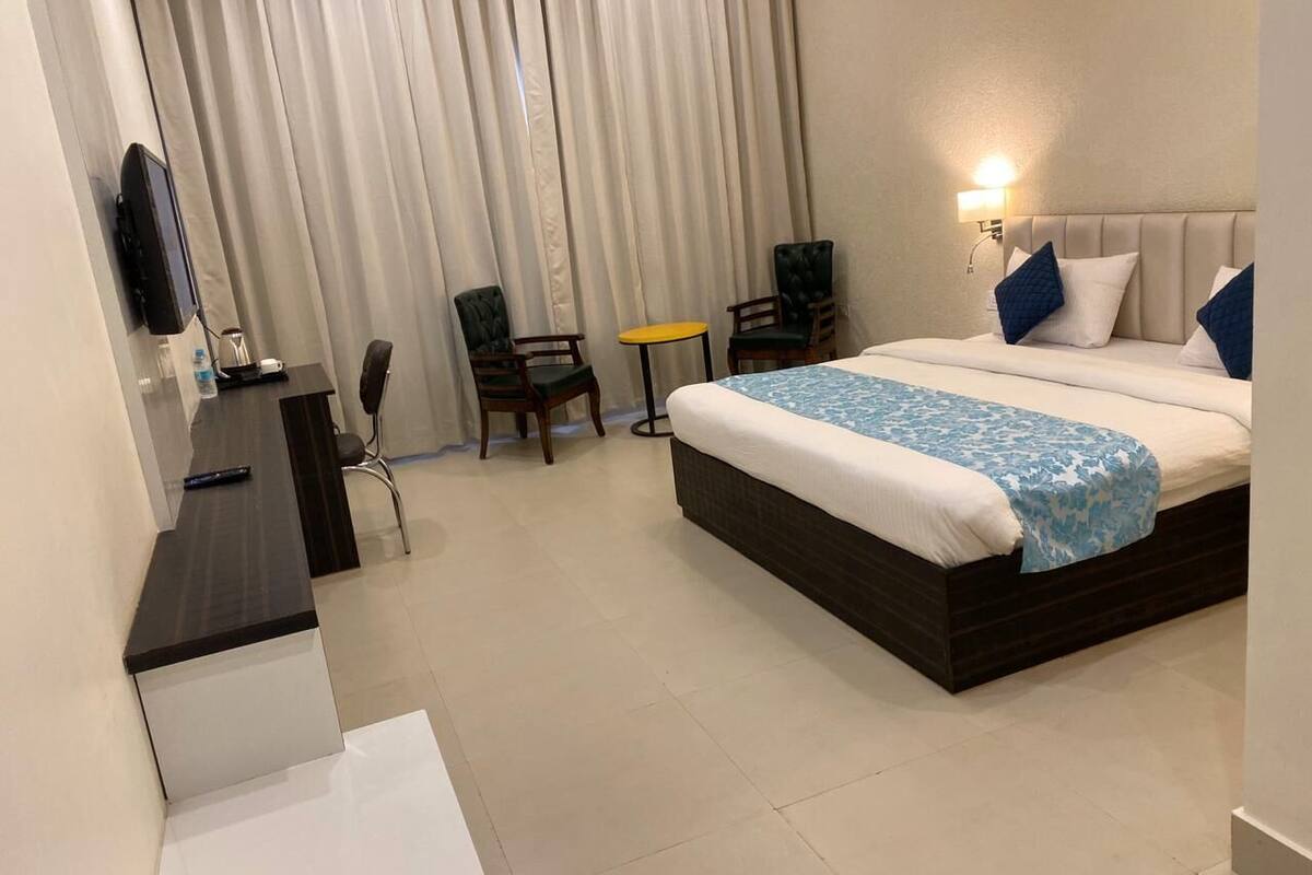 A hotel room with a bed, a desk, a chair, a small table, and a TV.