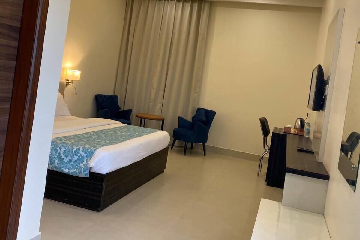 A hotel room with a bed, a desk, a chair, a ceiling fan, and a large window with curtains.