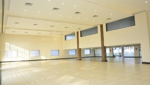 Un espacio interior amplio, bien iluminado, con techo alto, ventanas grandes y piso de baldosas.