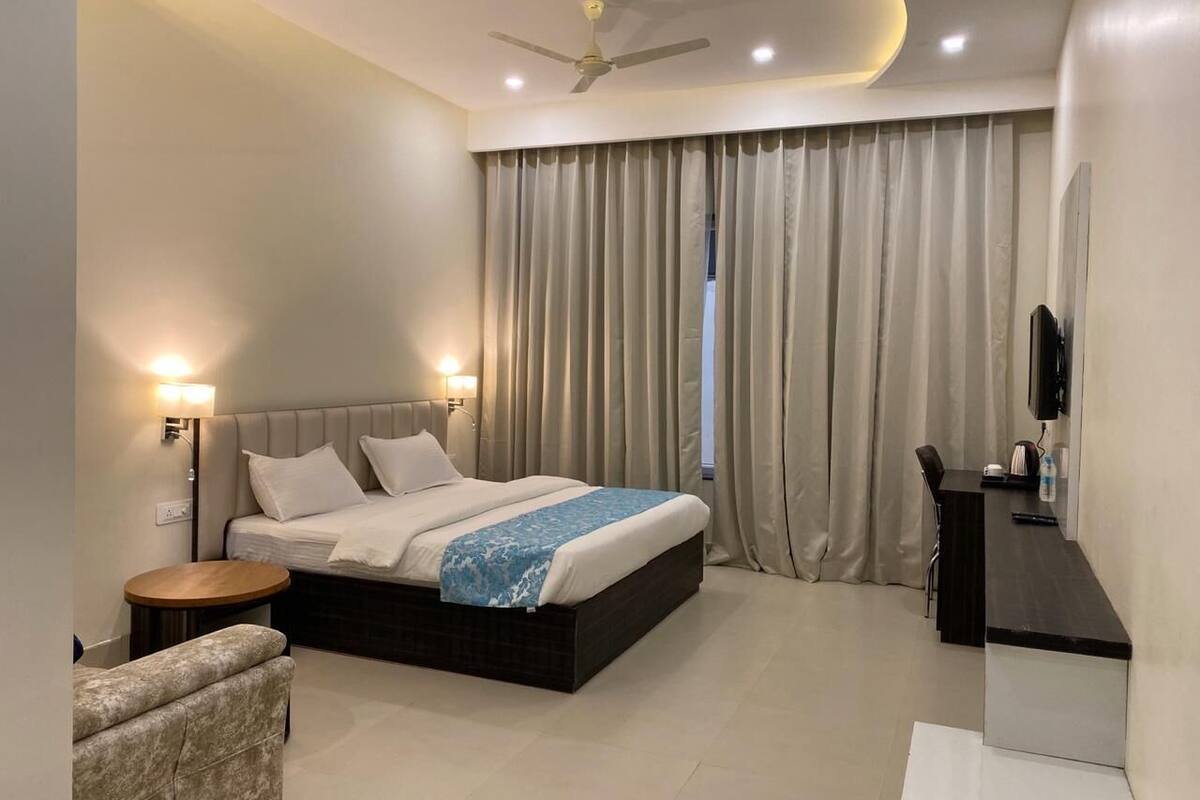 A hotel room with a bed, bedside tables, a desk, a chair, a TV, and a ceiling fan.