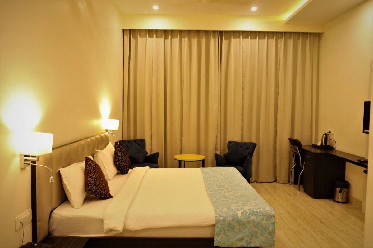 A hotel room with a bed, two chairs, a small table, a desk, and a TV.