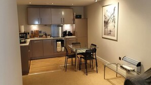 Une cuisine compacte dotée d’appareils électroménagers modernes, un coin repas avec une table et des chaises, et un radiateur fixé au mur.