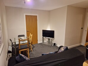 A compact living space with a TV, a dining table with chairs, a sofa, and a door. - Birmingham Ruby, 2 Bedroom Apartment (Birmingham)