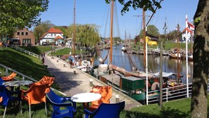 Ein Flussufer-Café mit Außenplätzen, eine Anlegestelle mit Booten und ein Gebäude mit rotem Dach.