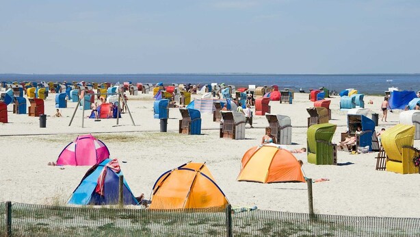 Ein Strand mit zahlreichen bunten Strandhütten und Zelten.