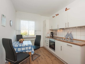 Une cuisine compacte avec une table et des chaises, une fenêtre ornée de rideaux légers et un mur recouvert de carreaux.