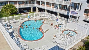 A hotel pool area with multiple pools, lounge chairs, and a sign for 'Tiffany The Sea'. - Nice 2 bedroom condo with pristine hardwood floors, free WiFi, and an outdoor pool located midtown and only a block to the beach! (Ocean City)