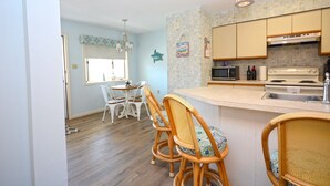 A kitchen with a central island, white chairs, a dining table, and a hanging light fixture. - Nice 2 bedroom condo with pristine hardwood floors, free WiFi, and an outdoor pool located midtown and only a block to the beach! (Ocean City)