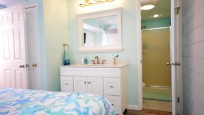 A bedroom with a bed, a vanity with a mirror, and a shower area. - Nice 2 bedroom condo with pristine hardwood floors, free WiFi, and an outdoor pool located midtown and only a block to the beach! (Ocean City)