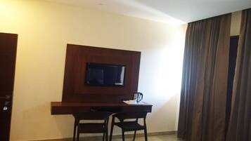 A room with a wooden desk, two chairs, a flat-screen TV mounted on the wall, and a large window with curtains.