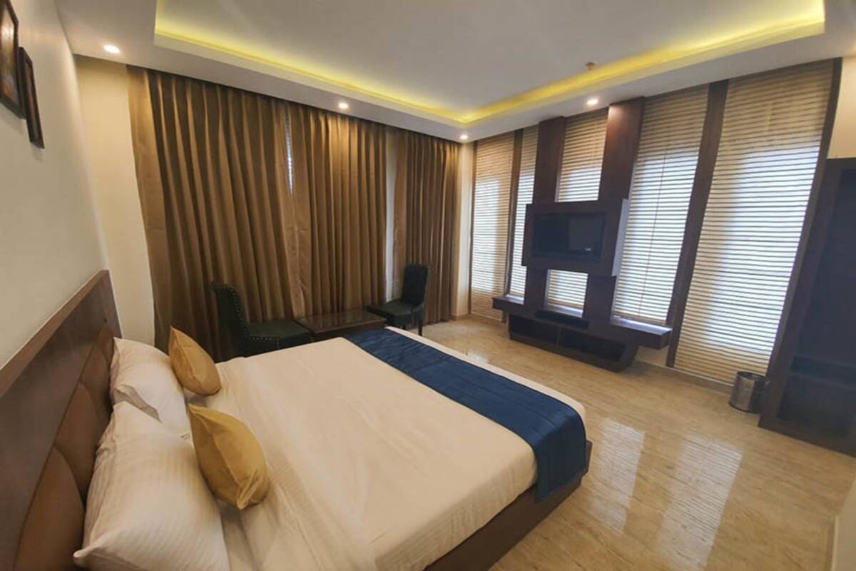 A hotel room with a large bed, a desk, a chair, a TV, and a window with blinds.