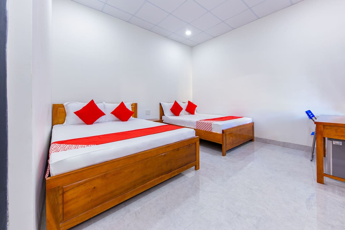 Habitación de hotel con dos camas de madera, ropa de cama blanca, almohadas rojas, un escritorio de madera y suelo de baldosas.