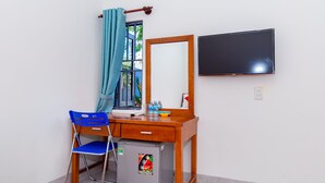 Una habitación pequeña con un escritorio de madera, una silla azul, un refrigerador compacto, un espejo y un televisor fijado en la pared.