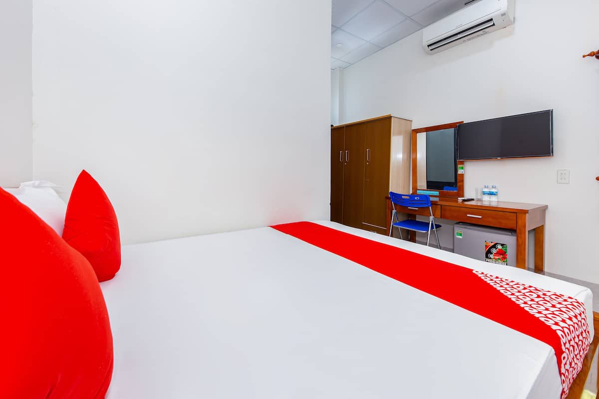 Una habitación de hotel con cama, un escritorio con silla, armario y unidad de aire acondicionado.