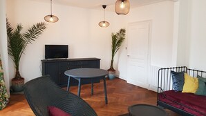 A living room with a sofa, a chair, a small table, and two potted plants. - Apartment 100 m² in a mansion (Munster)