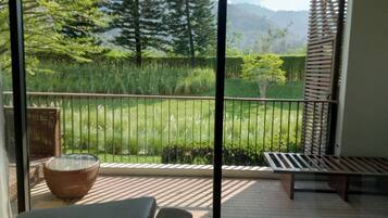 A balcony with a view of a grassy area and trees, a wicker chair, and a wooden bench.