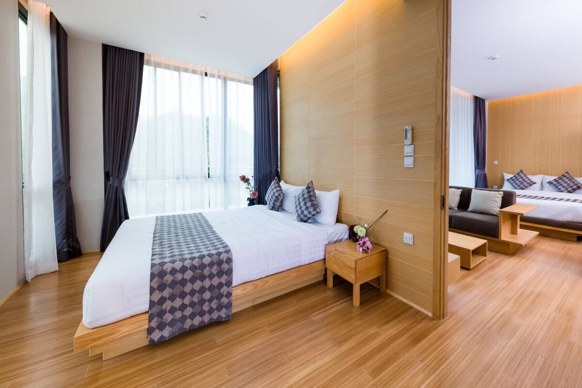 A modern hotel room with a large bed, a smaller bed, a sofa, and a desk.