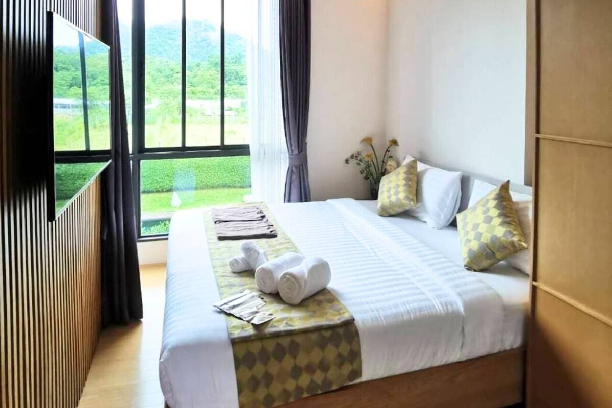 A hotel room with a large bed, a TV, and a view of greenery outside.