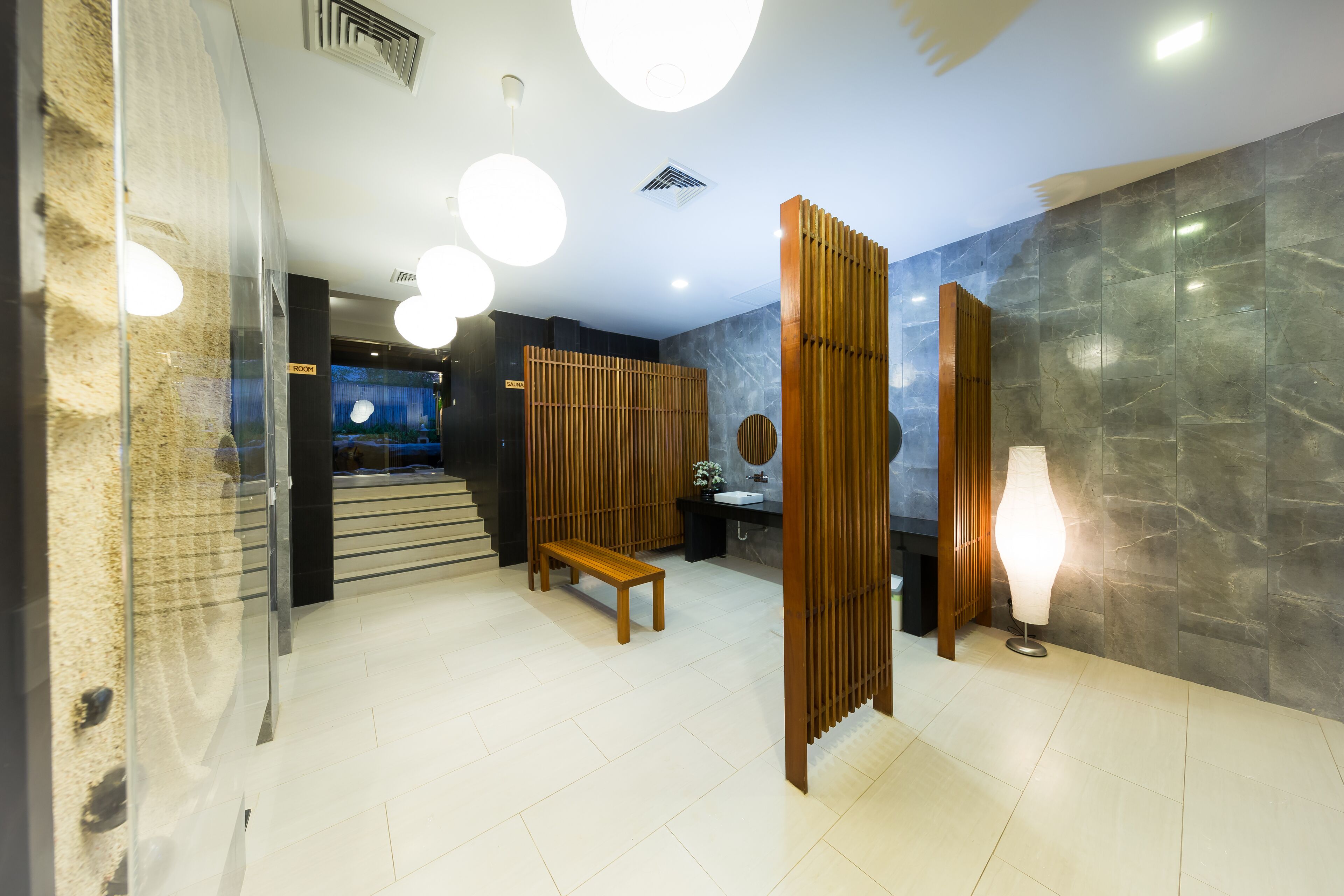 A modern lobby with a wooden bench, a reception desk, and a large wall with a circular mirror.
