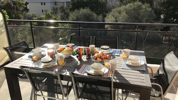 A dining table set outdoors with various dishes, cups, and a small figurine. - 3-room luxury apartment, fully renovated, ocean view, pool, beach within walking distance (Antibes)