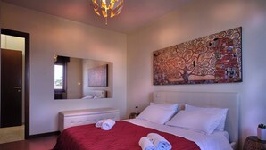 A hotel room with a large bed, a bedside table, a mirror, and a wall painting.