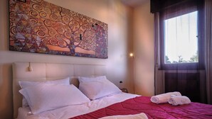 A hotel room with a large bed, white linens, a red bedspread, and a wall-mounted artwork.