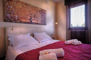 A hotel room with a large bed, white linens, a red bedspread, and a wall-mounted artwork.