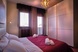 Quarto de hotel com cama, janela com cortinas, luminária na parede e vista para o exterior.