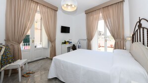 A bedroom with a large bed, beige curtains, a television on the wall, and a view of the outside. - Palazzo Gargano (Amalfi)