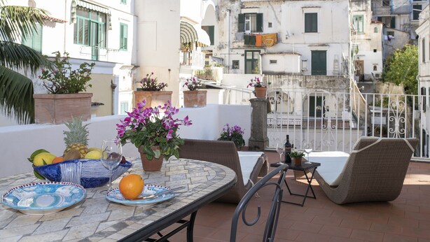 A terrace with a table set for dining, surrounded by wicker chairs, and potted plants. - Palazzo Gargano (Amalfi)