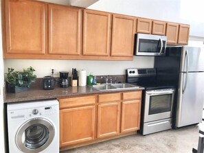 A kitchen with wooden cabinets, a microwave, a stove, a refrigerator, a sink, and a washing machine. - 303/C Little Italy double balcony Loft /Parking (San Diego)